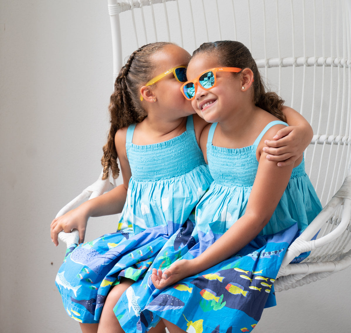 Two little girls wearing Sunnies polarized kids sunglasses in a yellow and orange transparent frame with reflective blue lenses