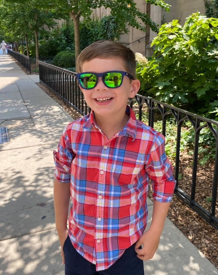 Young boy wearing Thank you Berry Punch polarized kids sunglasses in a transparent blue frame and green reflective lenses.