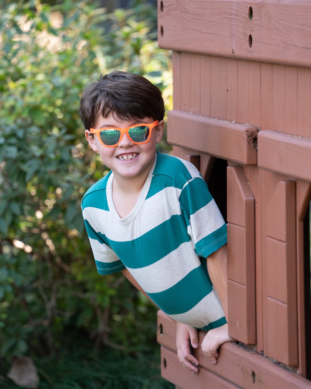 Little boy wearing polarized kids sunglasses by Sunnies shades in a transparent orange frame with reflective blue lenses.