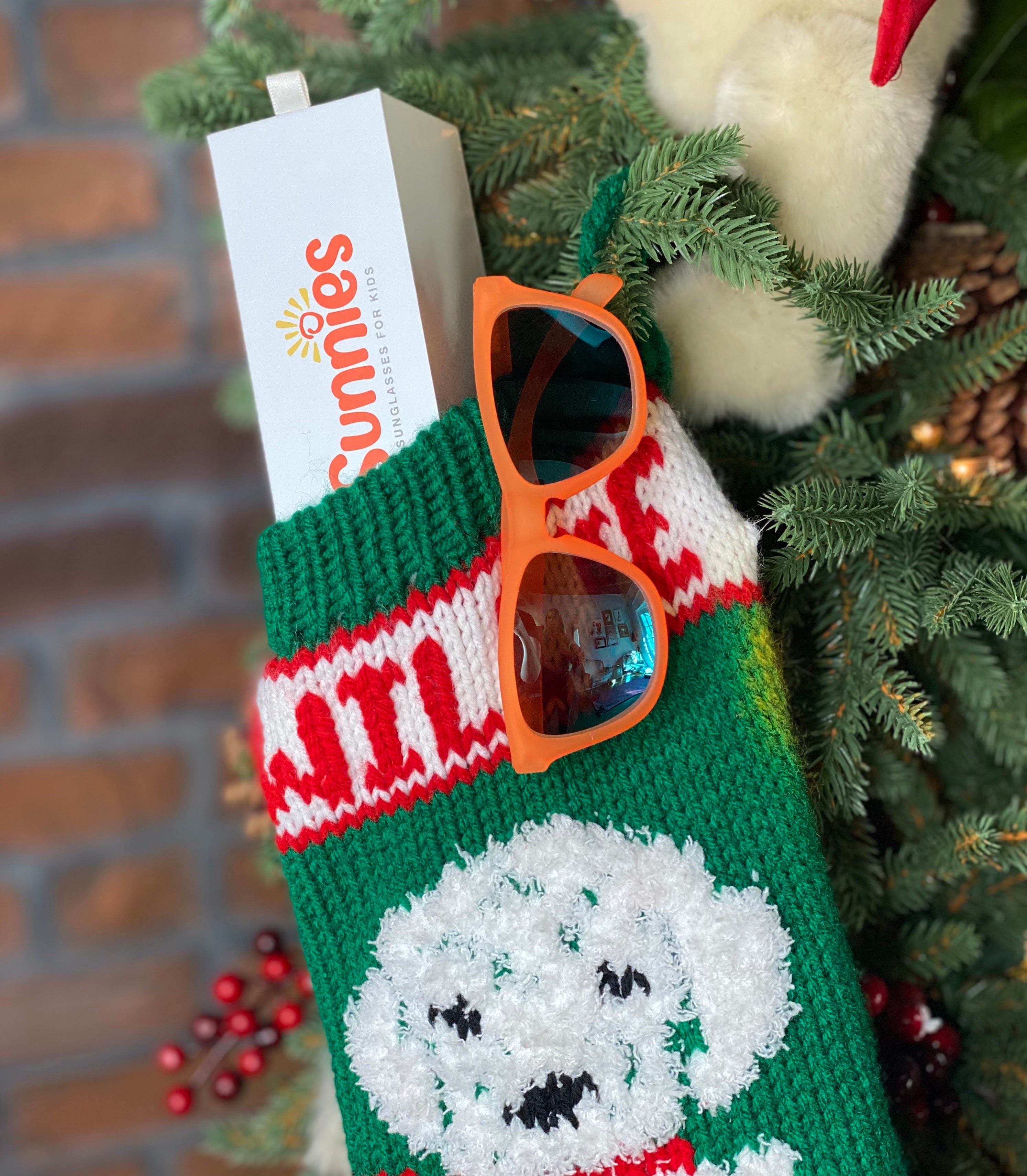 Christmas stocking with a pair of polarized kids sunglasses in an orange frame by Sunnies Shades sticking out of the stocking..
