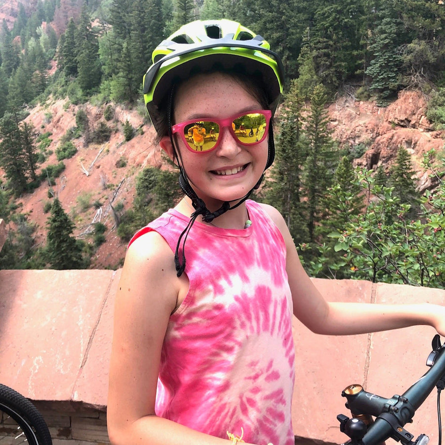 Girl on a bike wearing Sunnies polarized kids sunglasses in a pink frame with 100% UVA/UVB Protection