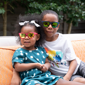 Little boy and toddler girl wearing Sunnies polarized kids sunglasses in a blue and pink frame.