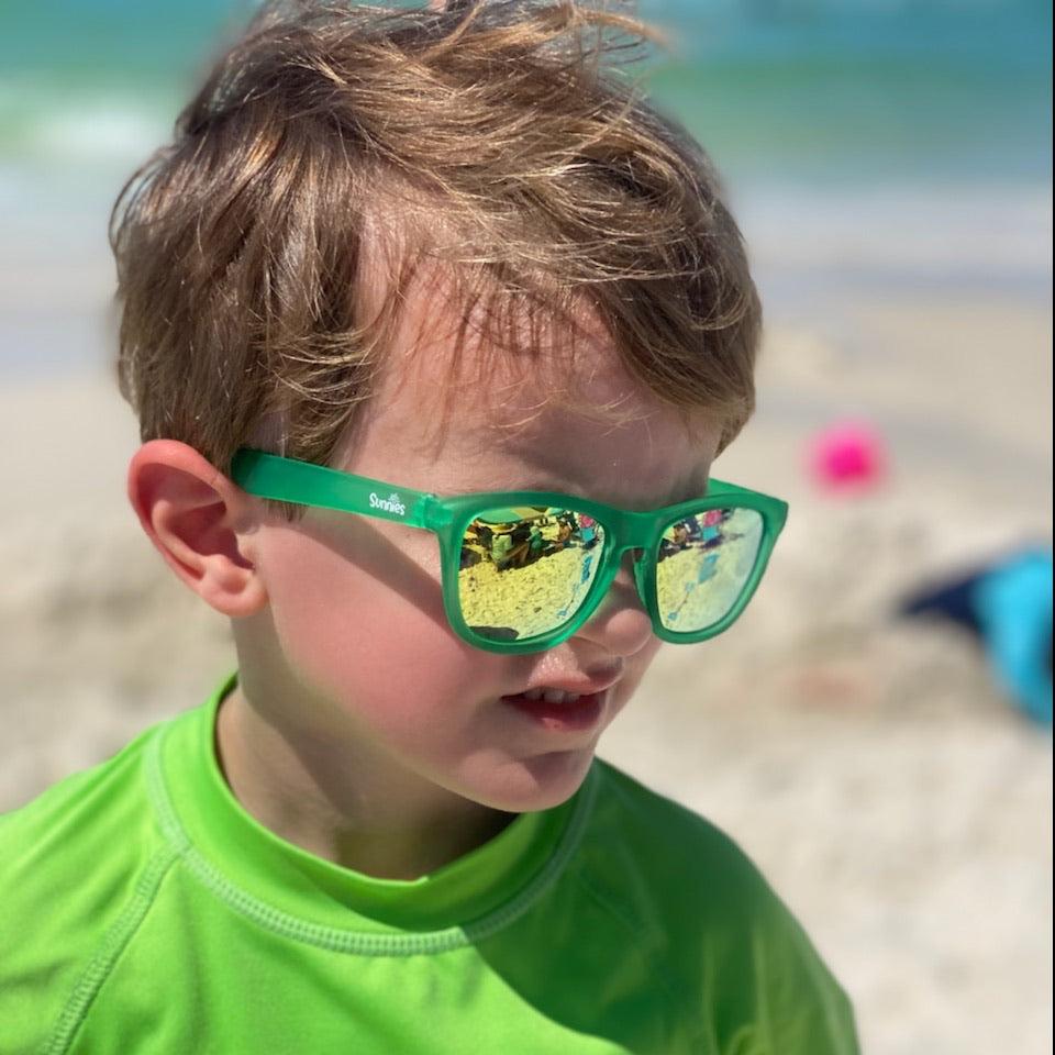 Little boy wearing polarized green sunnies at the beach with 100% UVA/UVB protection and an anti-slip material on the frame.