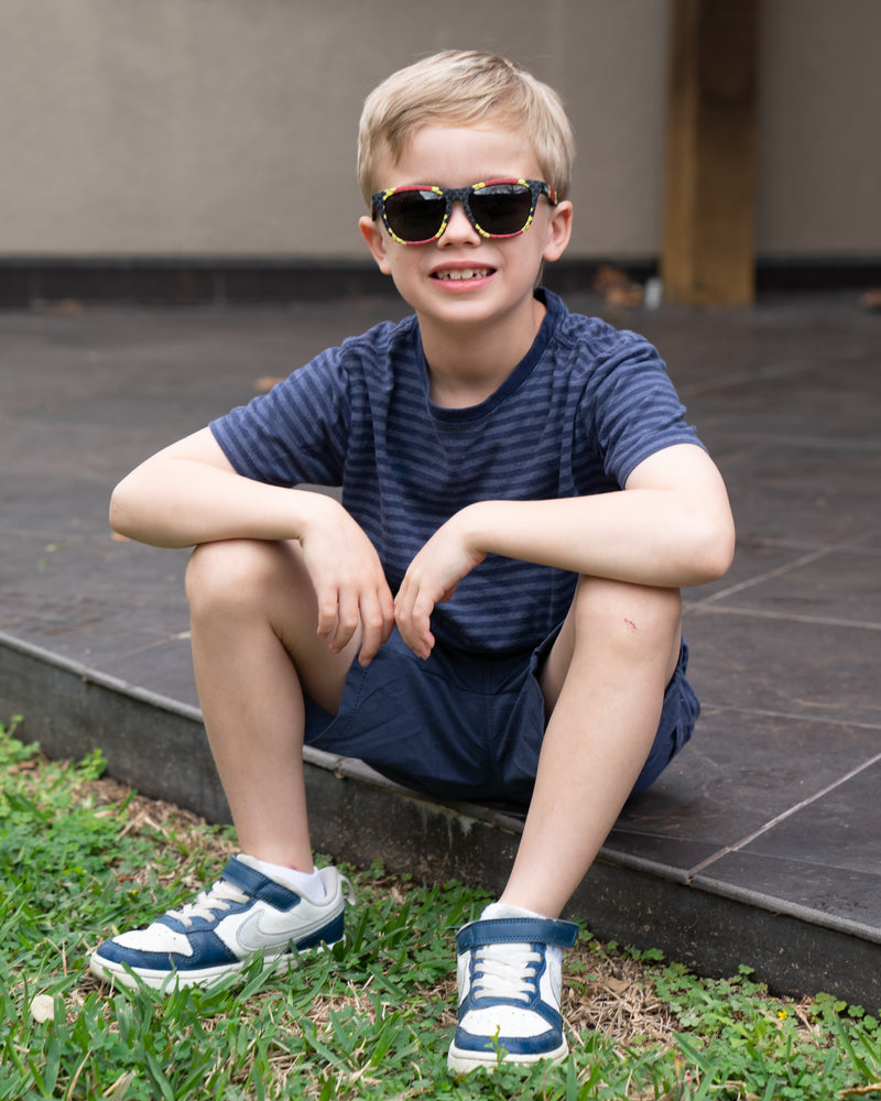 Little boy sitting outside wearing polarized kids sunglasses in a snake print frame.
