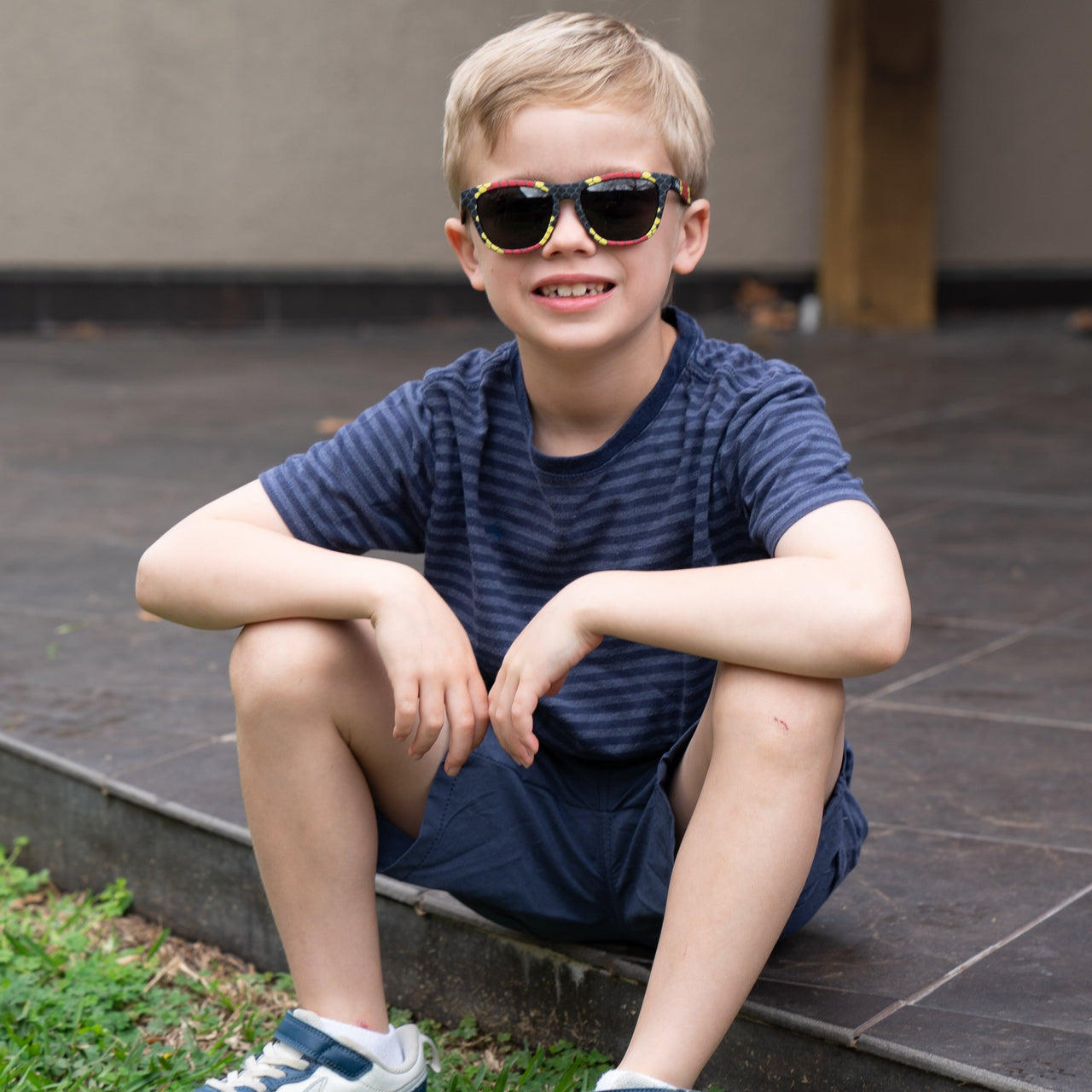 Little boy sitting outside wearing polarized kids sunglasses in a snake print frame.