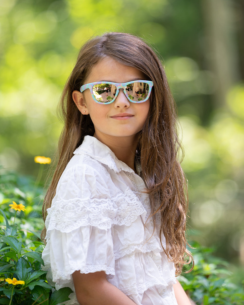 Close up image of young girl wearing Wild and Free frame with a pastel tie dye print and gold reflective polarized lenses.