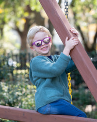 Little boy playing on a playground while wearing polarized kids sunglasses by Sunnies shades in a transparent purple frame and reflective purple lenses.