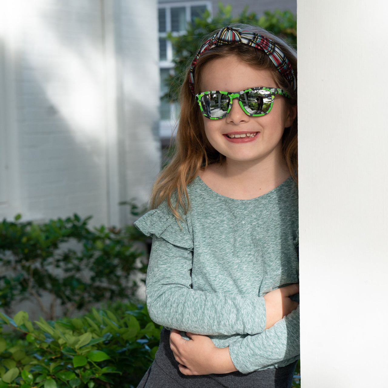 Little girl wearing sunnies shades kids polarized sunglasses in a green camo print with silver reflective lenses.