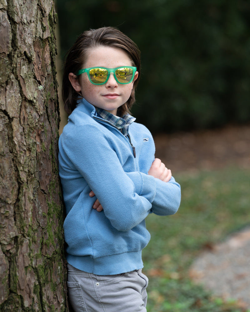 Little boy wearing Sunnies shades kids polarized sunglasses in a transparent green frame with gold reflective lenses.