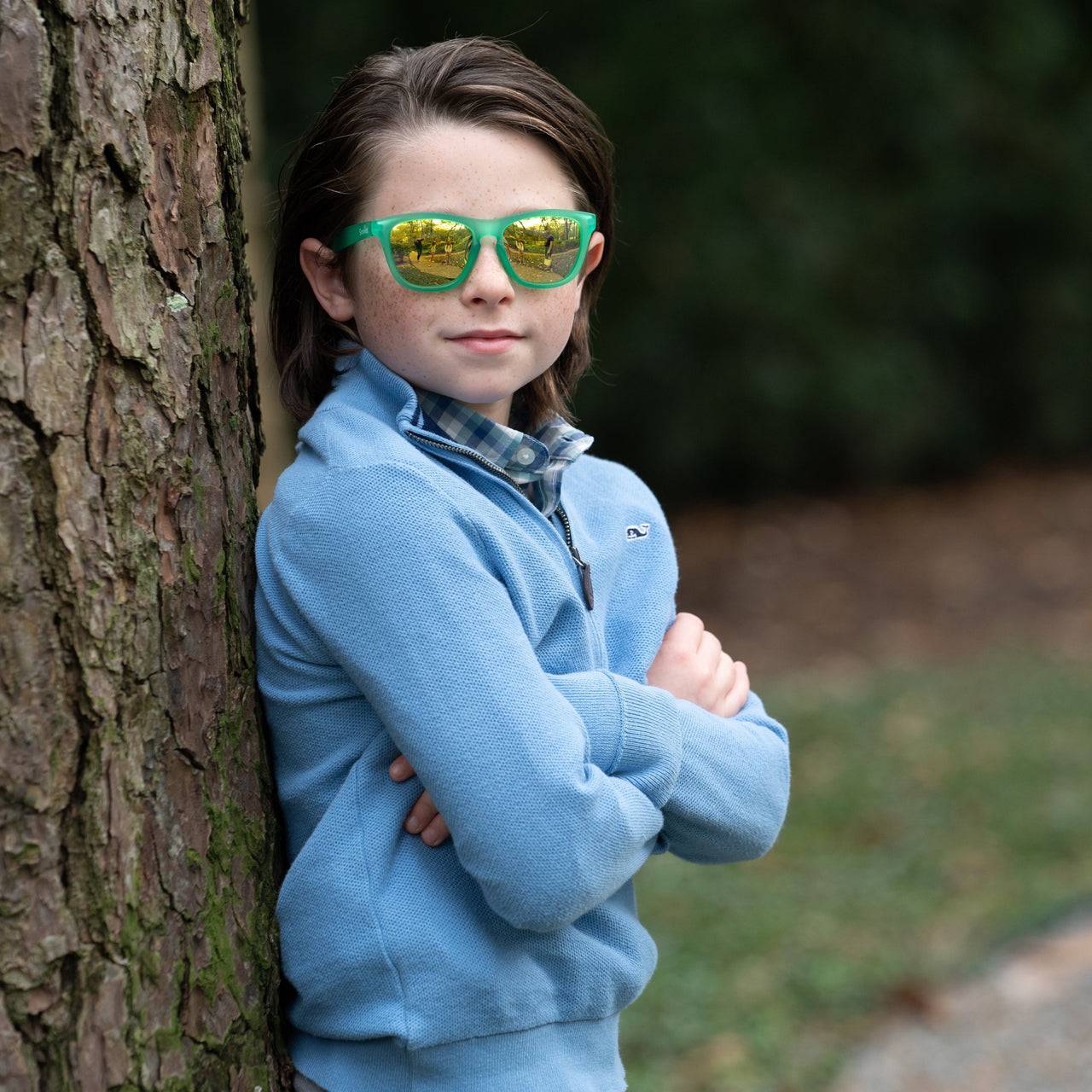 Little boy wearing Sunnies shades kids polarized sunglasses in a transparent green frame with gold reflective lenses.