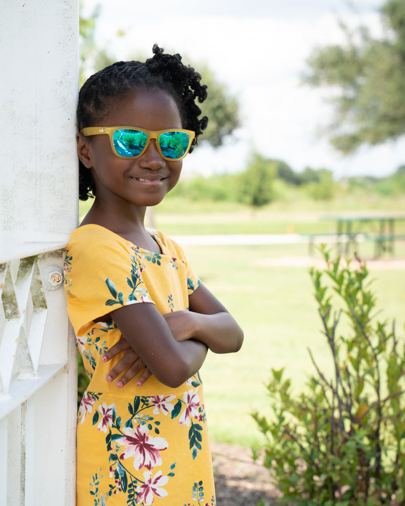 Little girl wearing sunnies shades polarized kids sunglasses in a transparent yellow frame with reflective blue lenses.