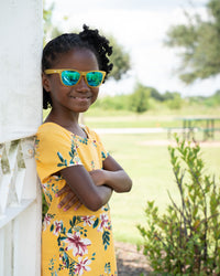 Thumbnail for Little girl wearing sunnies shades polarized kids sunglasses in a transparent yellow frame with reflective blue lenses.