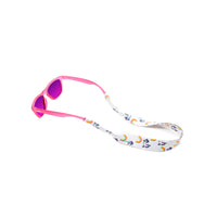 Kids sunglass strap in a unicorn and rainbow print attached to a pair of sunnies kids sunglasses in pink