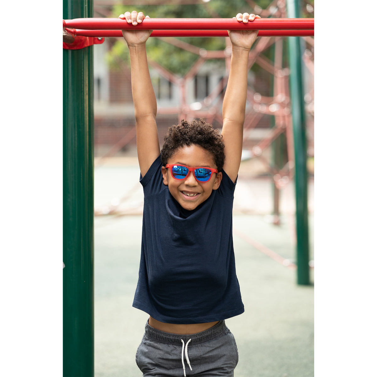 Little boy hanging from monkey bars wearing sunnies red polarized kids sunglasses